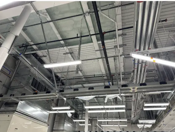 Interior of a large commercial space with plastic sheeting covering the floor and walls, scaffolding, and exposed insulation in the process of being installed.