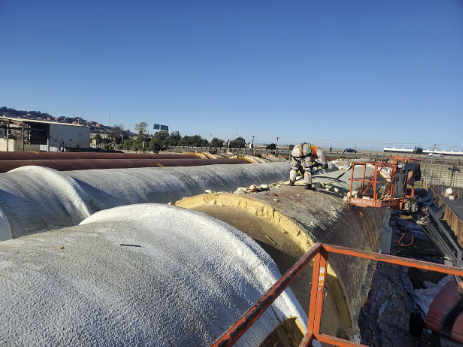  Workers on a lift spraying foam insulation on large industrial tanks. 