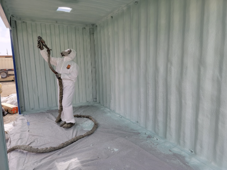  Contractor in protective gear spraying foam insulation inside a container.

              