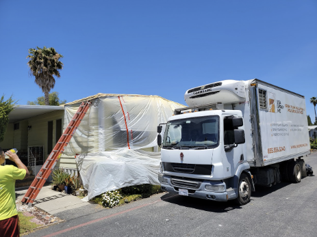 Spray foam insulation truck parked next to a house covered in protective plastic sheeting.  

              