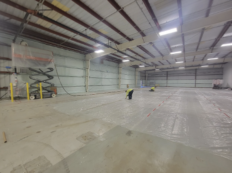 Interior view of a warehouse with workers installing insulation on the floor, demonstrating USA Spray Me's capability in commercial insulation projects.