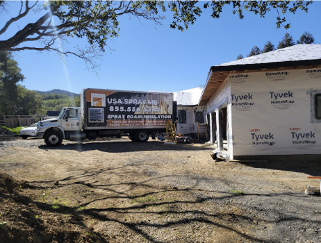  'USA Spray Me truck parked at a residential construction site with Tyvek-wrapped walls, illustrating the company's insulation services for homes.'



              