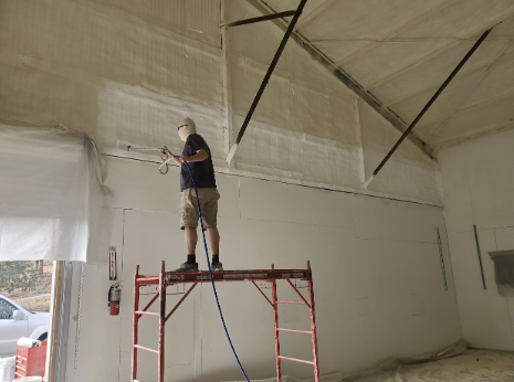  A worker standing on a scaffold, applying spray foam insulation to the high walls of a large custom home in San Francisco.
                        