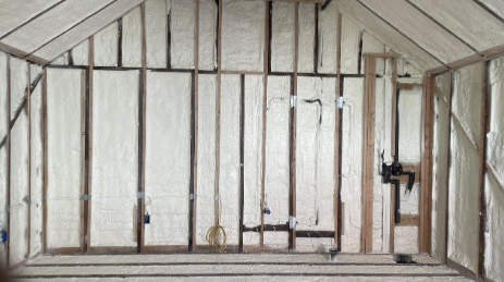  Wine cellar walls and ceiling with spray foam insulation applied, exposing wooden studs and electrical wiring. 