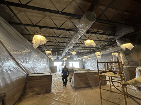   A construction site with walls and lighting fixtures covered in protective plastic sheeting, and a worker walking through the area.
                     