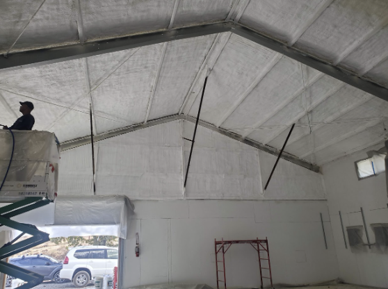  
   Worker on a lift applying spray foam insulation to the walls of a large recycling facility.


   