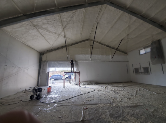  
                     Technician applying spray foam insulation to the ceiling of a recycling center.


                     