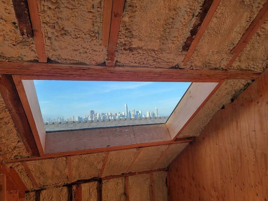  


                     Spray foam insulation applied under a roof with a skylight, overlooking a city skyline.





                     