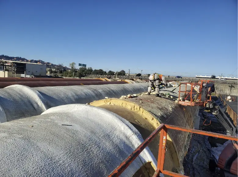 Technicians applying spray foam insulation on large industrial tanks to enhance energy efficiency and protect against weather elements.