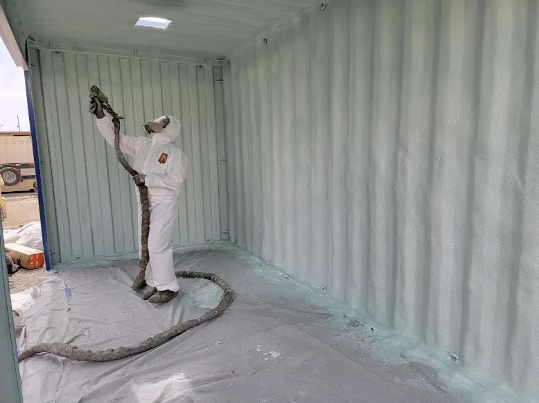 A professional contractor applying spray foam insulation inside a container for optimal thermal efficiency.