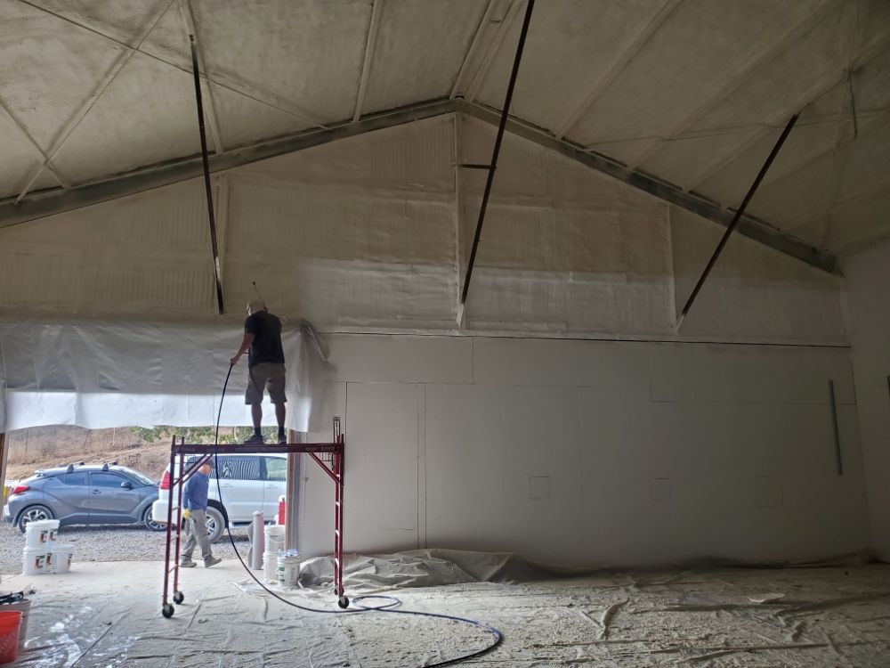  
               Worker applying spray foam insulation to a high ceiling using a scaffold.





      
      
      
               