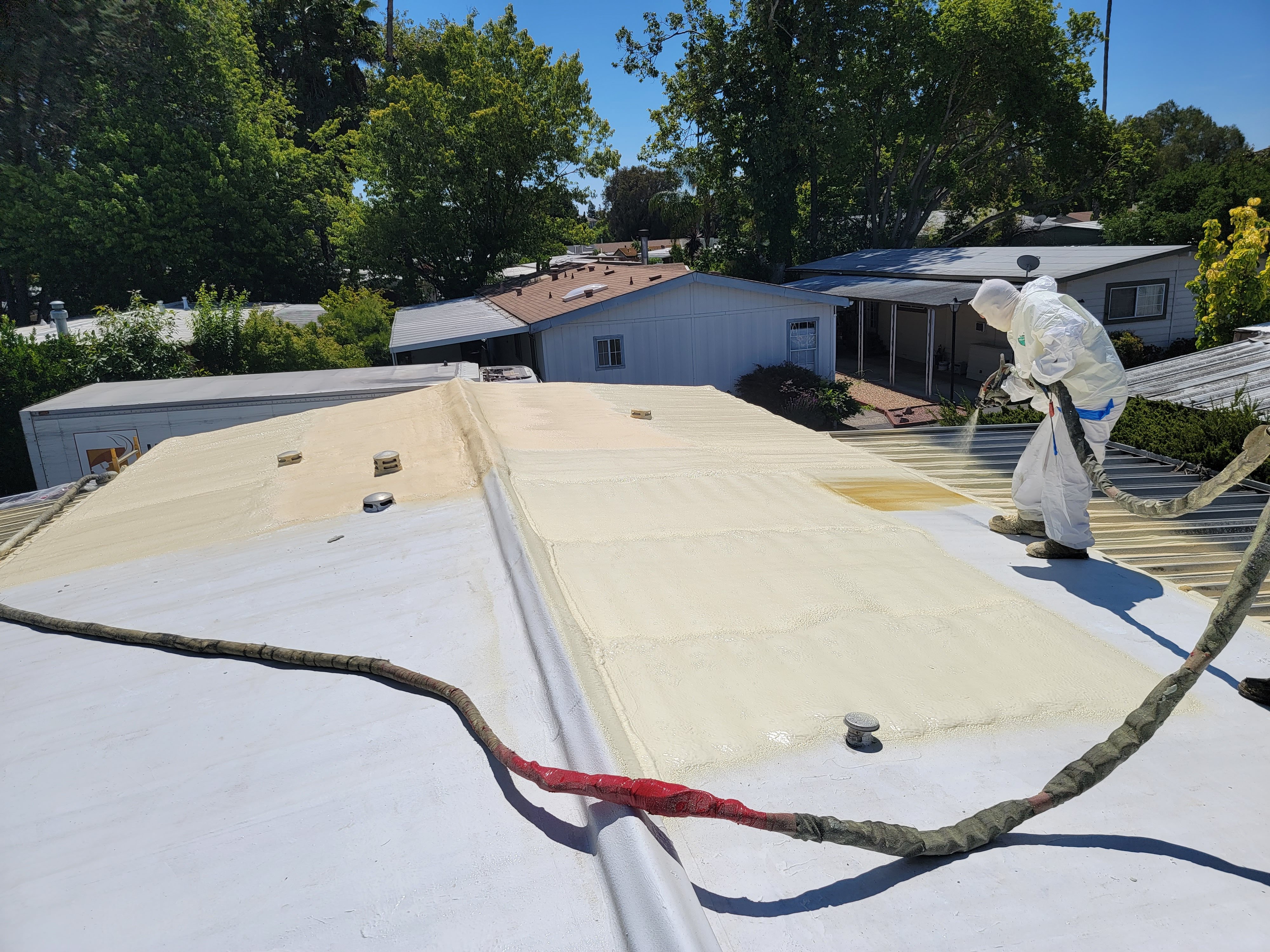  


                     Worker in protective gear applying foam roofing on a flat roof in a residential area.






                     