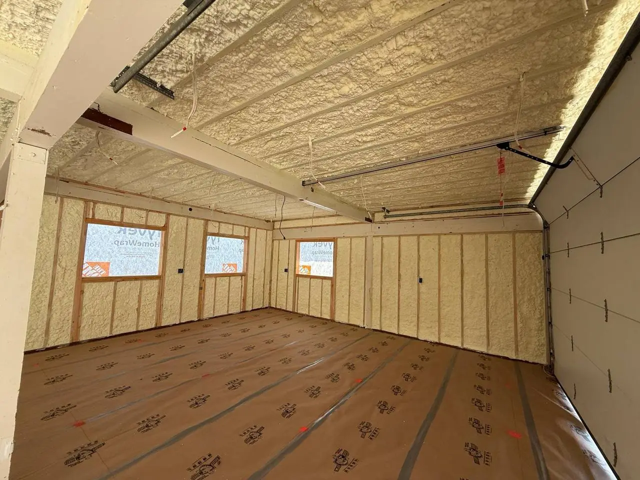 Interior of a building under construction in Walnut Creek with closed-cell spray foam insulation applied to walls and ceiling, wooden studs and protective floor covering visible.