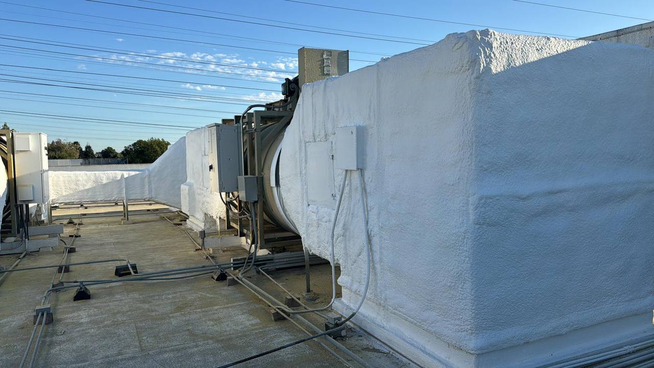 Interior of a building under construction in Hayward with spray foam insulation applied to walls, visible wooden studs, metal framing, and a plywood staircase leading to an upper level.