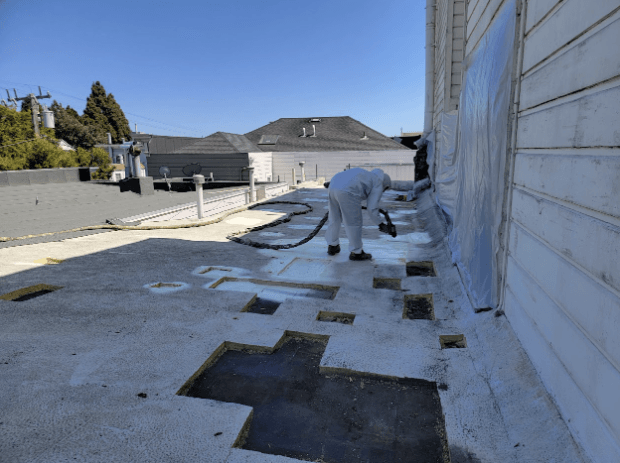 Workers applying spray foam insulation to a flat roof on a sunny day in San Jose, improving waterproofing and insulation properties.