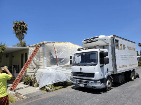Spray foam insulation truck parked next to a house covered in protective plastic sheeting.