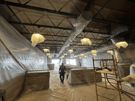 A construction site with walls and lighting fixtures covered in protective plastic sheeting, and a worker walking through the area.