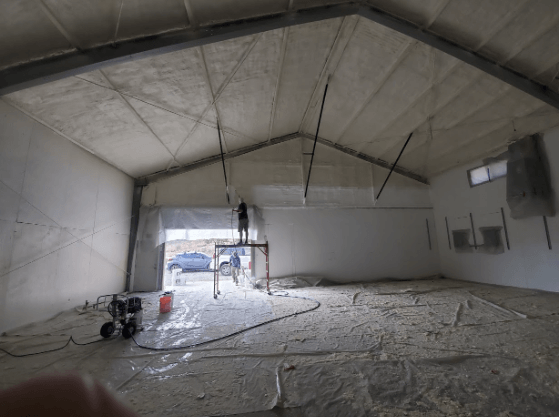 Technician applying spray foam insulation to the ceiling of a recycling center.