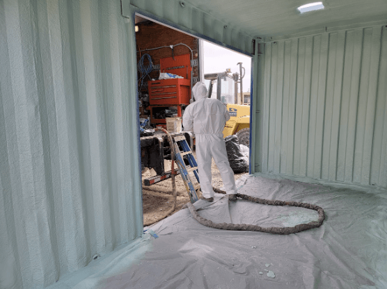 Worker in protective gear applying spray foam insulation to the walls of a medicine storage.