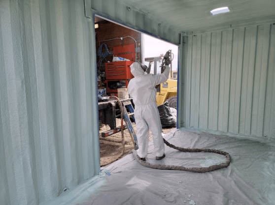Technician applying spray foam insulation inside a storage container, designed for medicine storage in California.