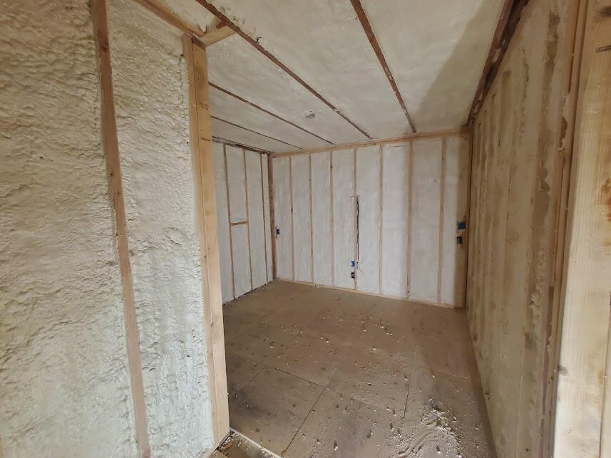 Interior room with spray foam insulation applied to walls and ceiling between framing.
