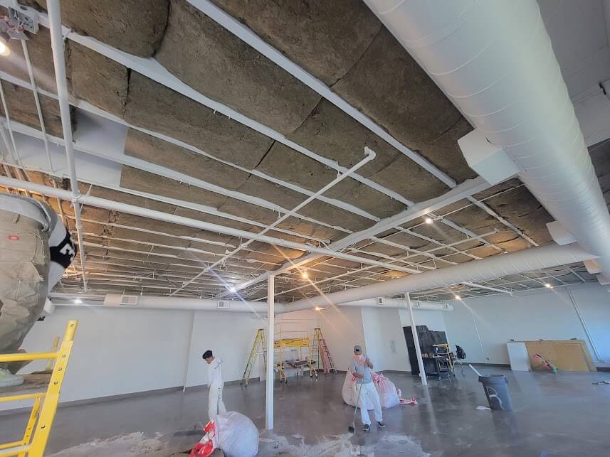 Workers installing mineral wool insulation on an exposed ceiling.