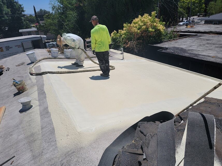 Workers applying spray foam insulation on a rooftop.
