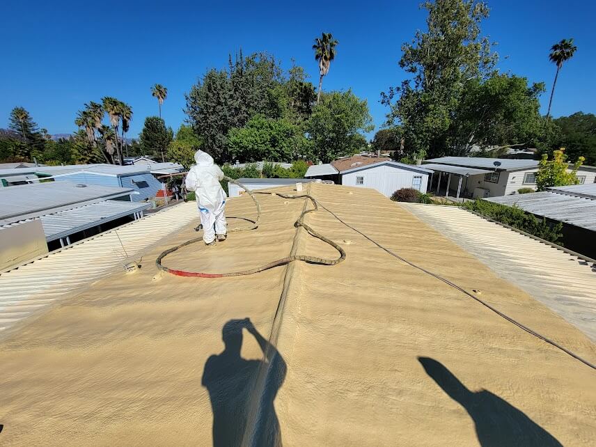 Worker in protective gear spraying foam roofing on a residential roof.