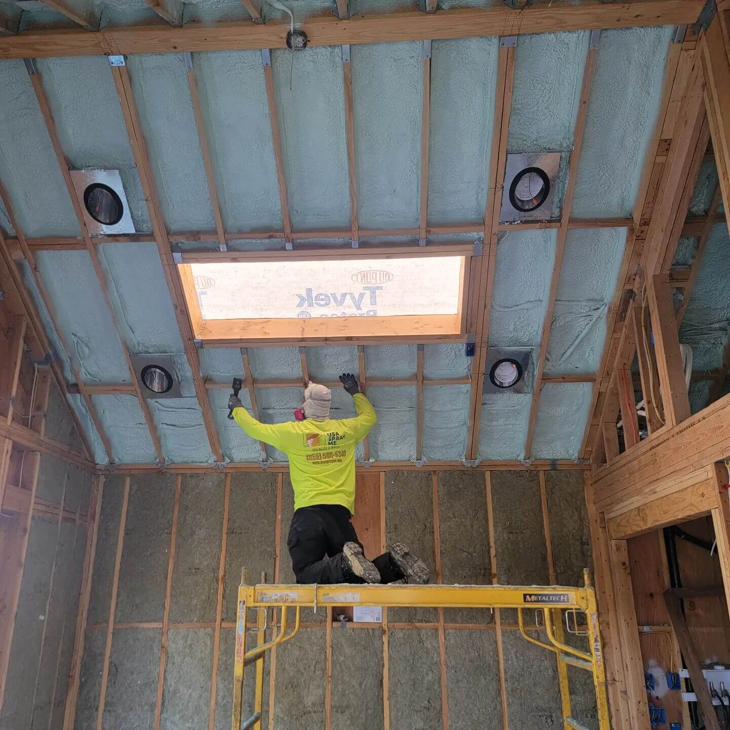Technician installing spray foam insulation around a skylight ceiling.