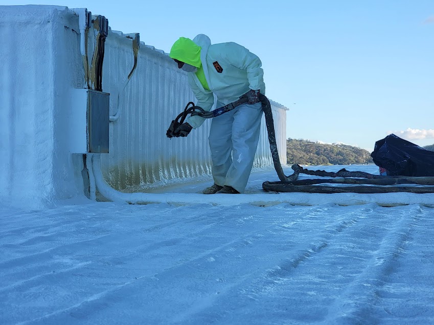 Worker applying spray foam insulation on a roof.