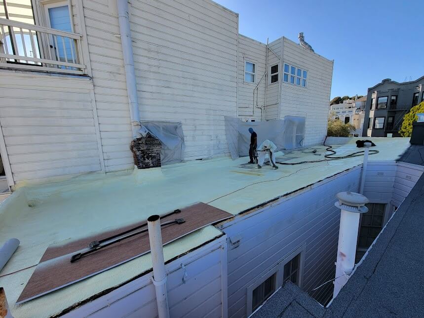 Contractors applying spray foam insulation on a rooftop.
