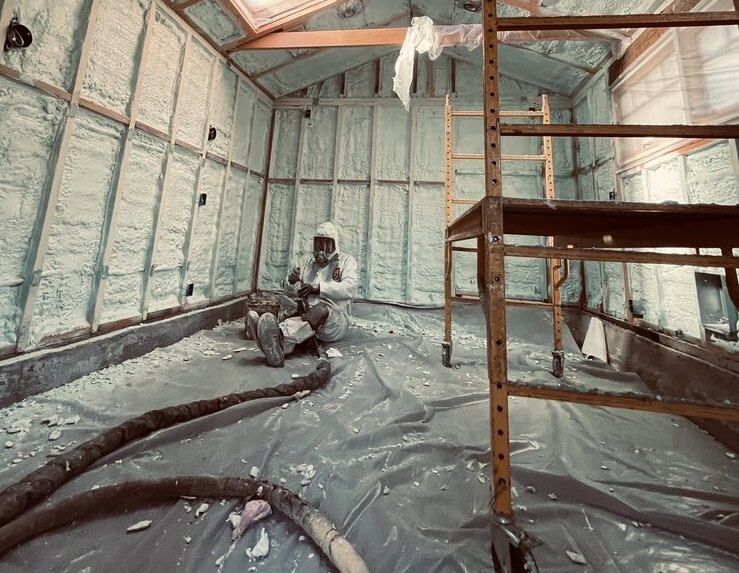USA Spray Me worker in a protective suit seated after applying spray foam insulation on walls.