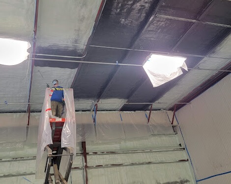 Technicians installing commercial insulation in a large open space.