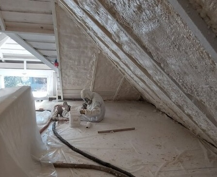  Worker in protective gear applying spray foam insulation to an attic. 