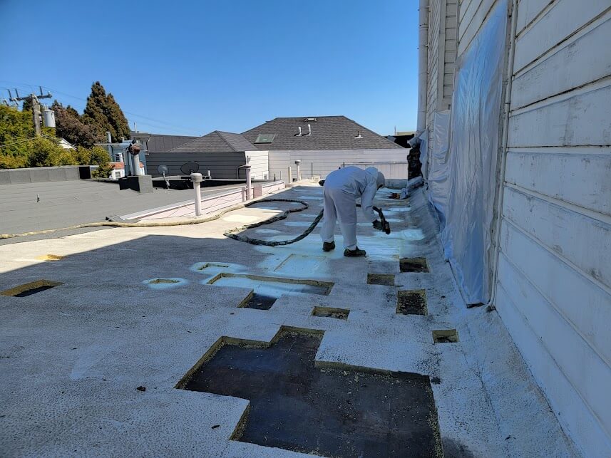 Worker applying spray polyurethane foam insulation to a residential rooftop.