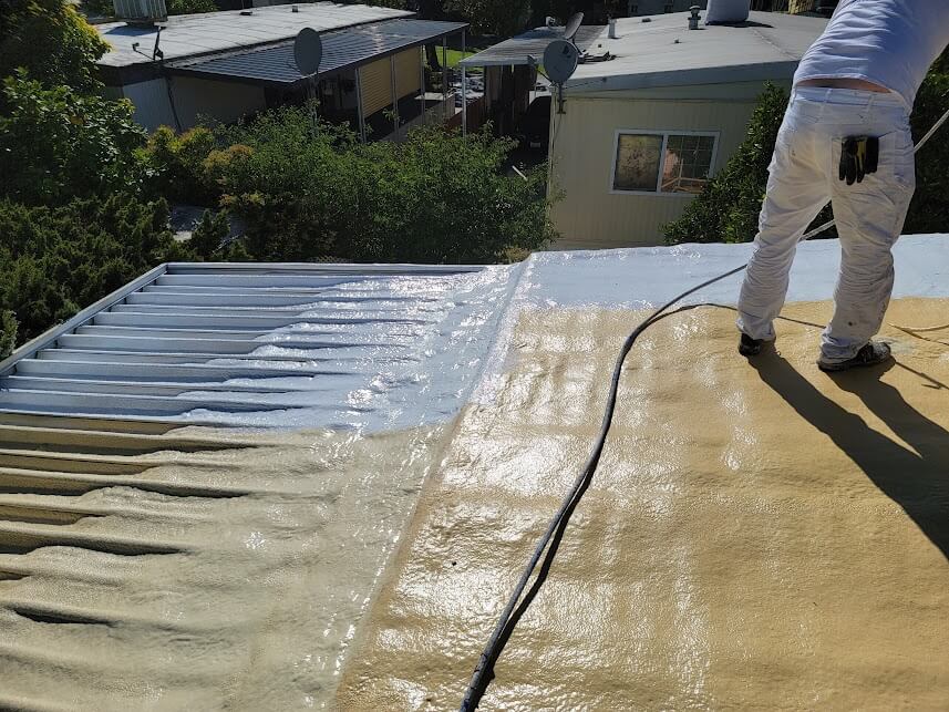  Worker applying spray polyurethane foam insulation on a low slope roof. 