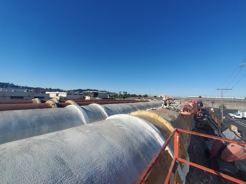 Workers applying SPF insulation on a large cold storage tank under clear skies.