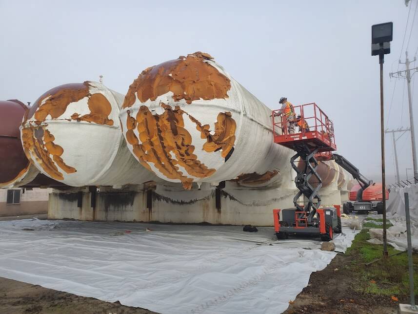 A USA Spray Me worker applying spray polyurethane foam insulation to a storage tank.