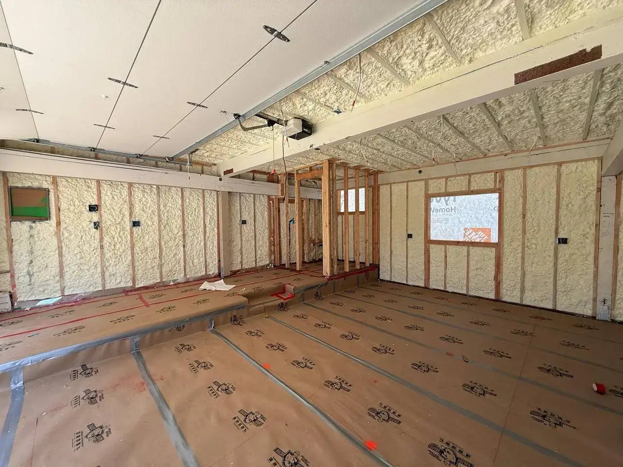 Interior of a building under construction in Walnut Creek with spray foam insulation applied to walls and ceiling, wooden studs and protective floor covering visible.